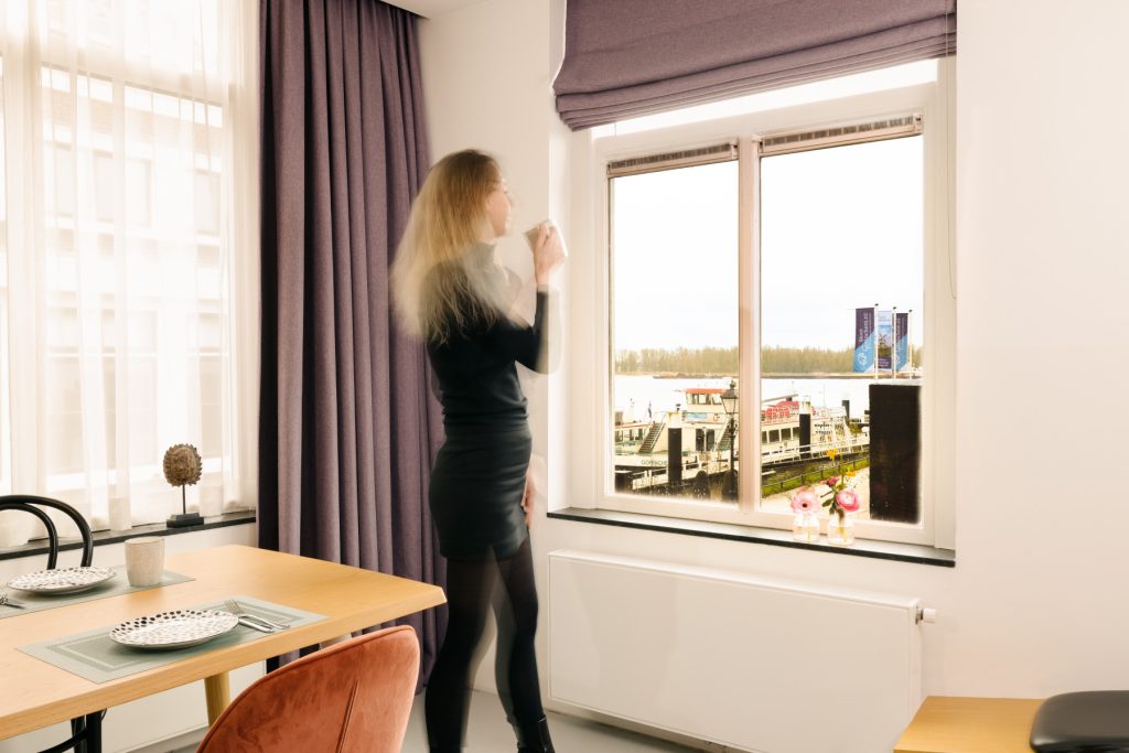 Model looks out window overlooking Outside Watergate longstay suite 15 hotel Gold and Silver